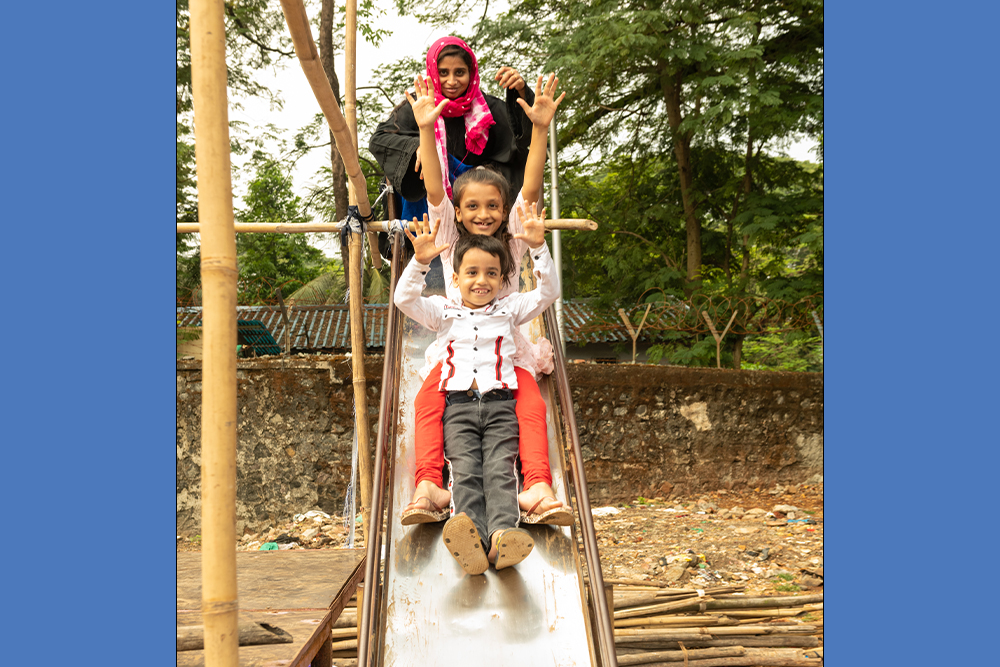 Humera smiling and going down the slide with her mother and brother at the playground