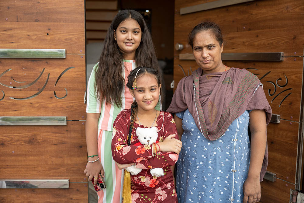 Bhumika smiling and holding a Smile Train teddy bear with her sister and mother Jyoti after cleft surgery