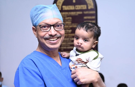 Dr Subodh smiling and holding a cleft-affected baby
