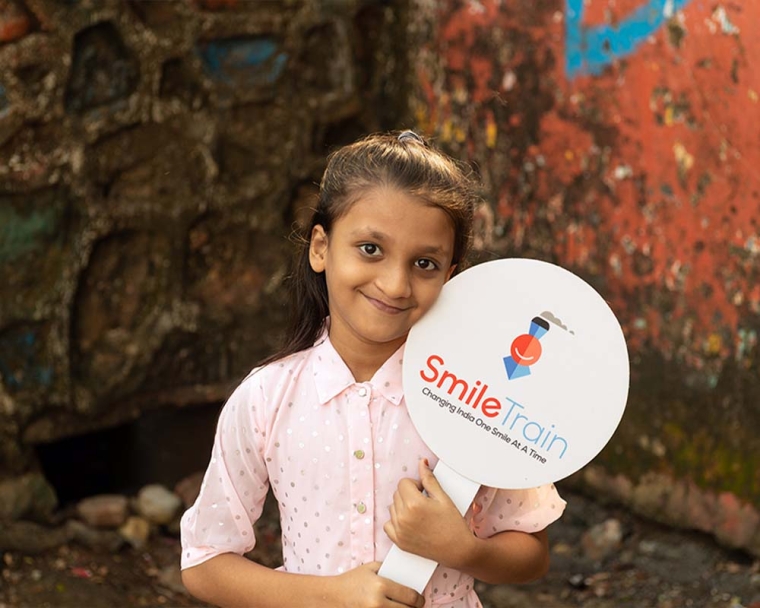 Humera smiling and holding a Smile Train sign after cleft surgery