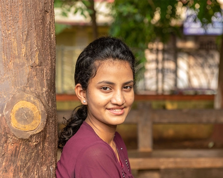 Bhargavi smiling and standing against a tree after cleft surgery