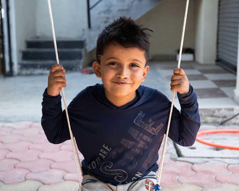 Abhay smiling and sitting on a swing after cleft surgery